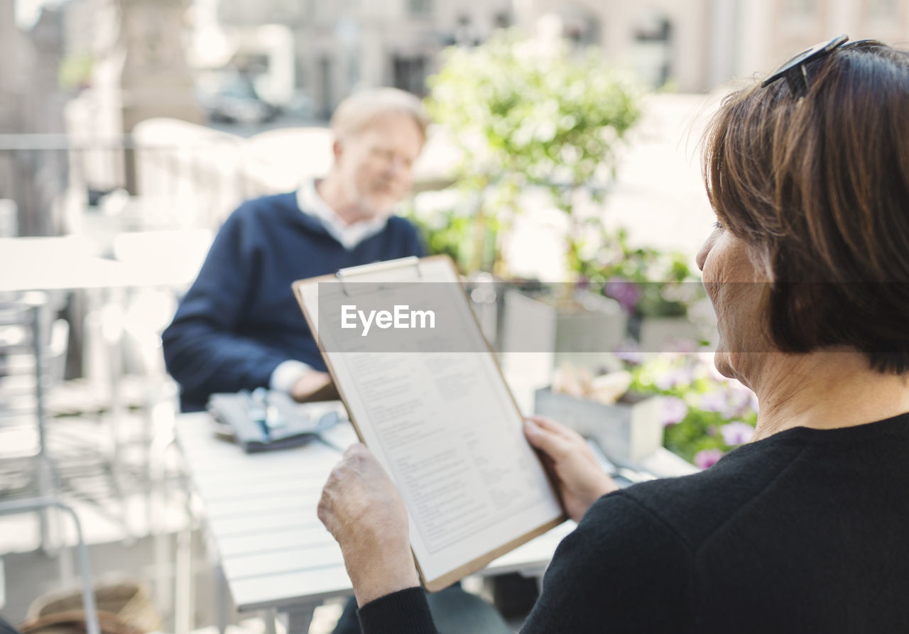 Rear view of woman reading menu while man sitting at sidewalk cafe