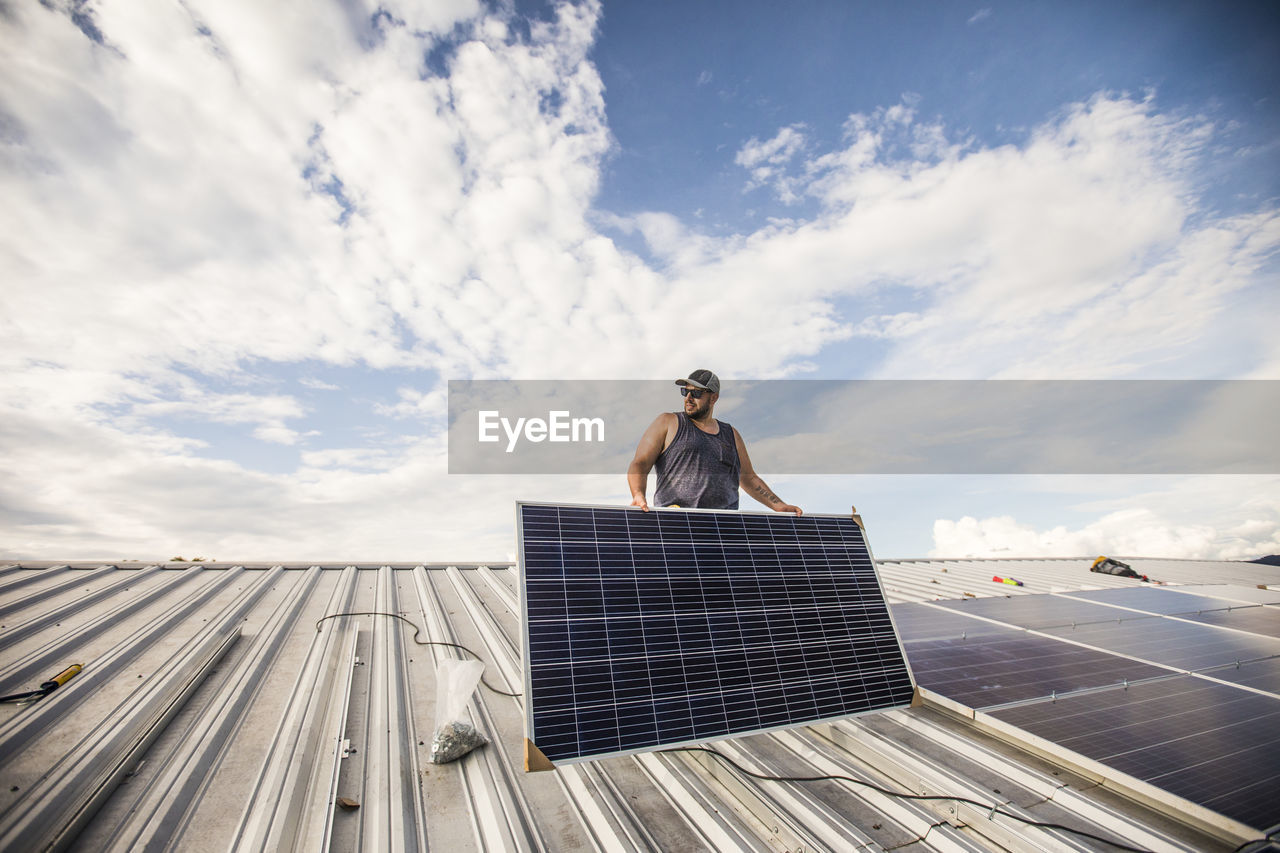 Low angle of construction worker installing solar panels on roof.