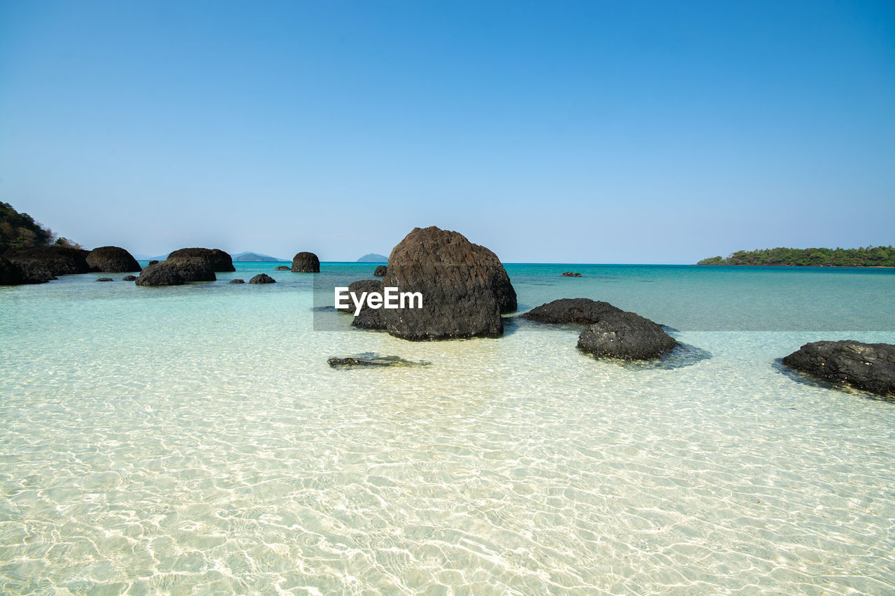 Rocks on beach against clear blue sky