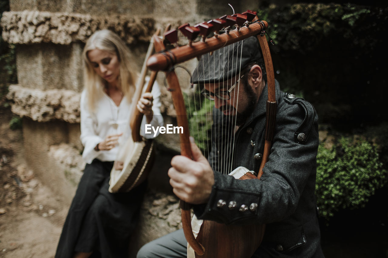 Male and female playing lyra instrument in public park