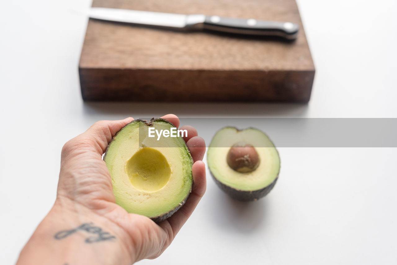 Cropped hand holding chopped avocado over white background