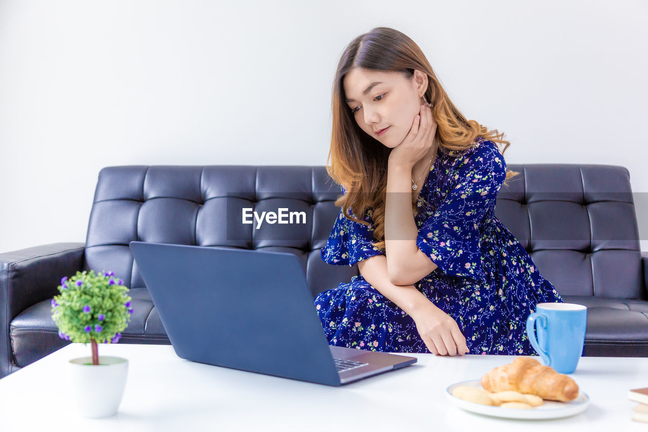 YOUNG WOMAN USING PHONE WHILE SITTING ON TABLE