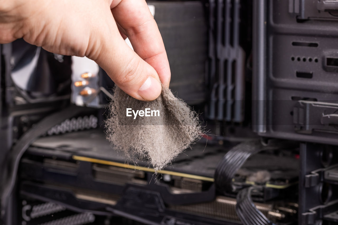 Bare caucasian hand holding dust clog in front of opened pc case during maintenance