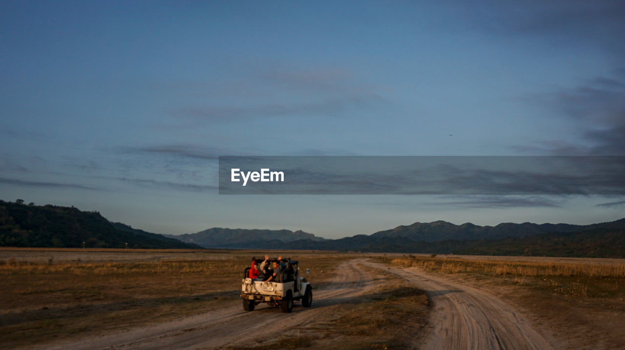 PEOPLE RIDING VEHICLE ON ROAD AGAINST SKY