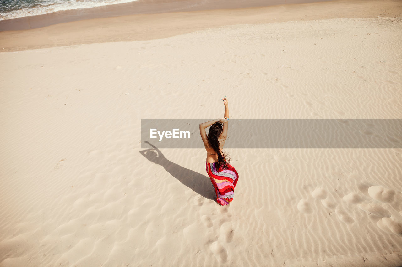 Rear view of woman with arms raised standing on sandy beach