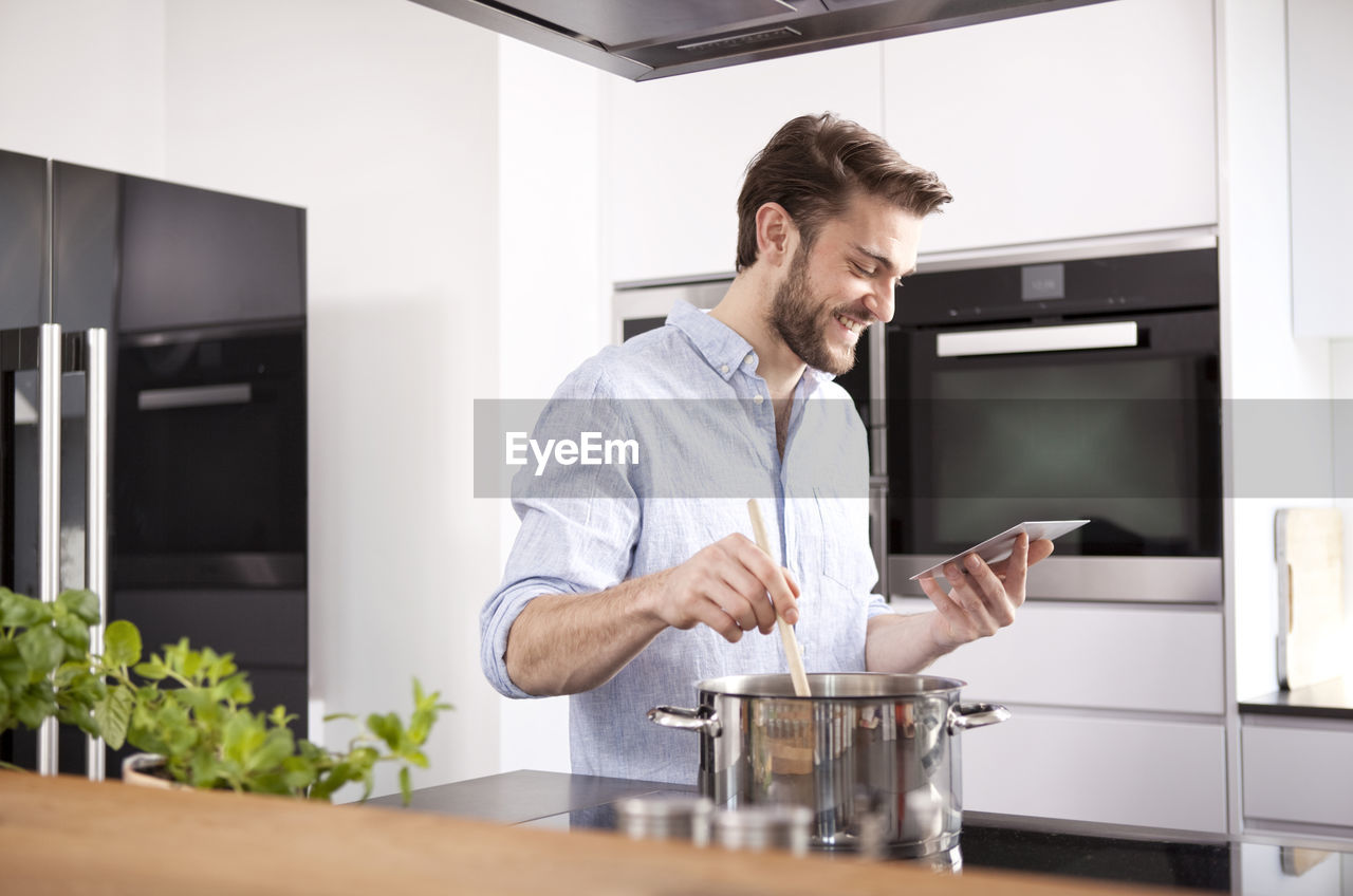 Young man looking at with mini tablet while cooking