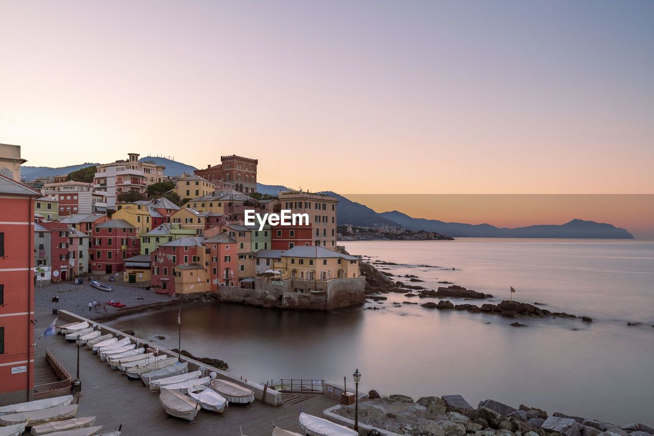 buildings by sea against sky during sunset