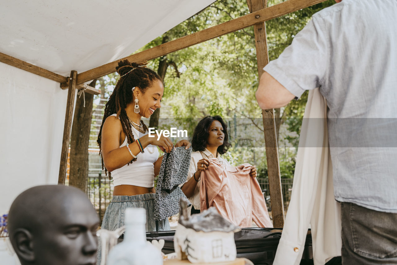 Female partners holding clothes while communicating with customers at flea market