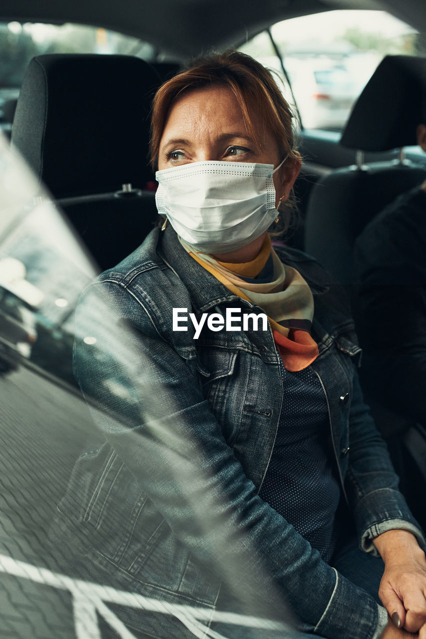 Woman sitting in a car wearing the face mask to avoid virus infection
