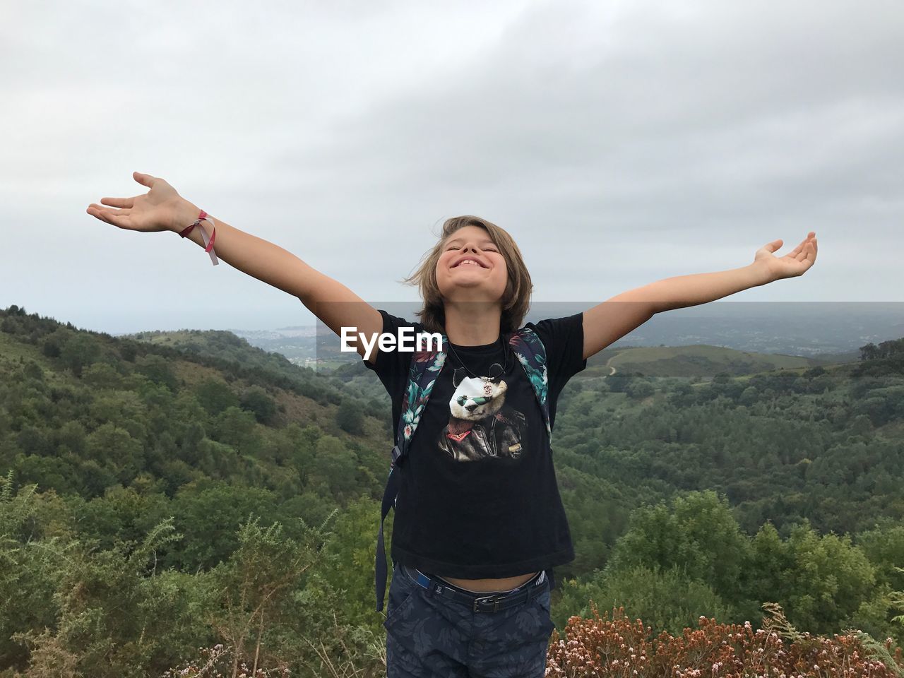 Carefree boy with arms outstretched standing on mountain against sky