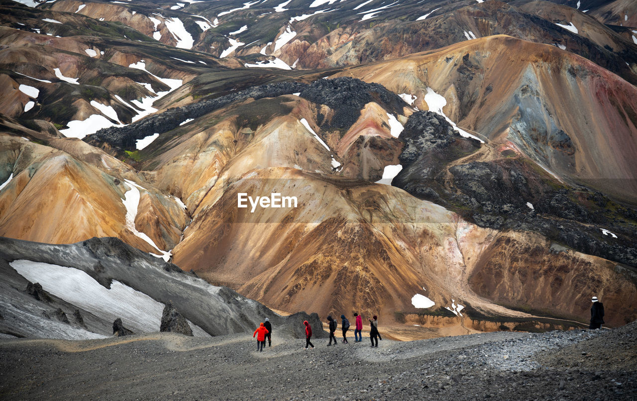 A group of hikers walking down a mountain with colorful volcanic mountains in the background.