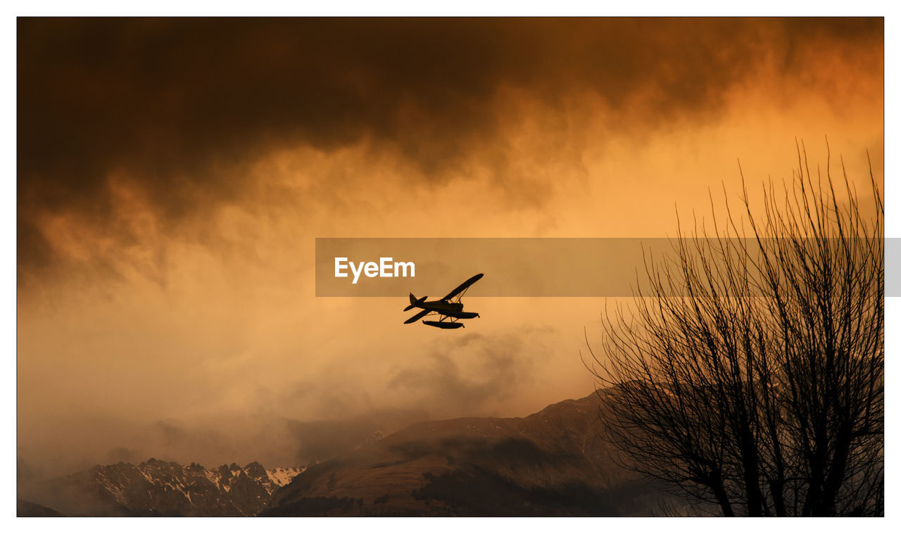 Silhouette plane flying against cloudy sky