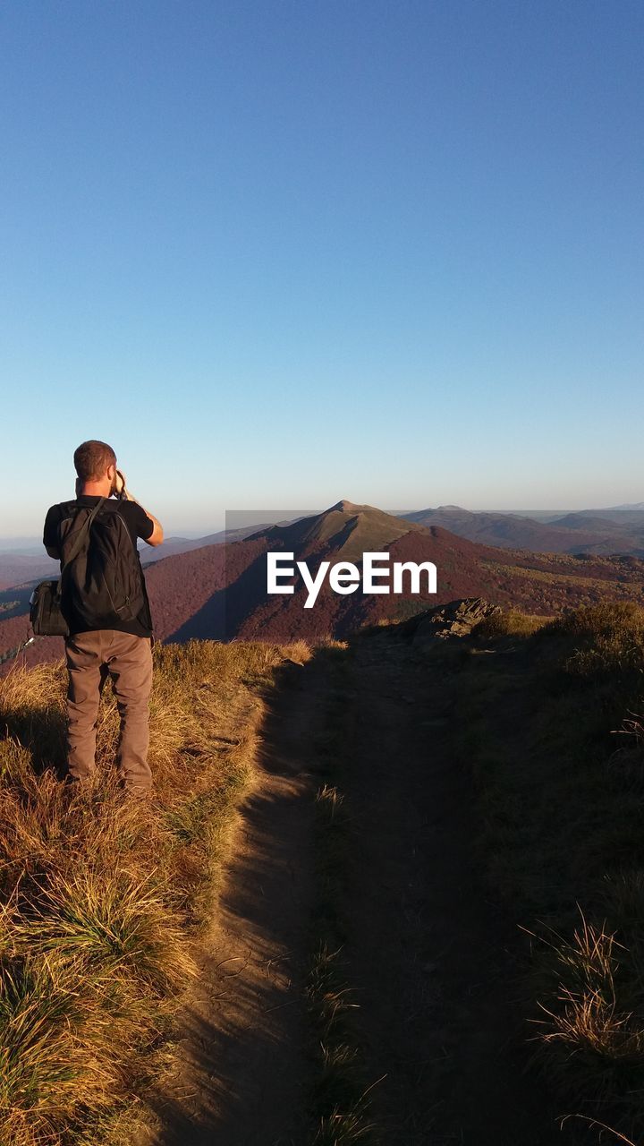 REAR VIEW OF MAN LOOKING AT LANDSCAPE AGAINST CLEAR SKY