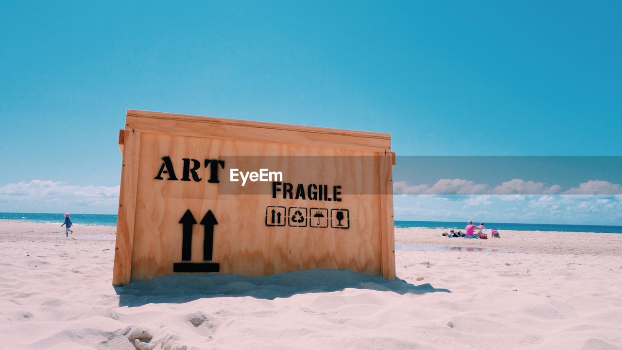 Wooden box with text at sandy beach on sunny day