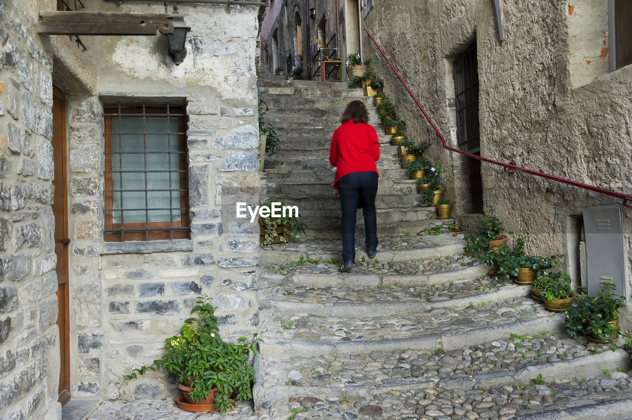 Woman walking up narrow stairs along walls