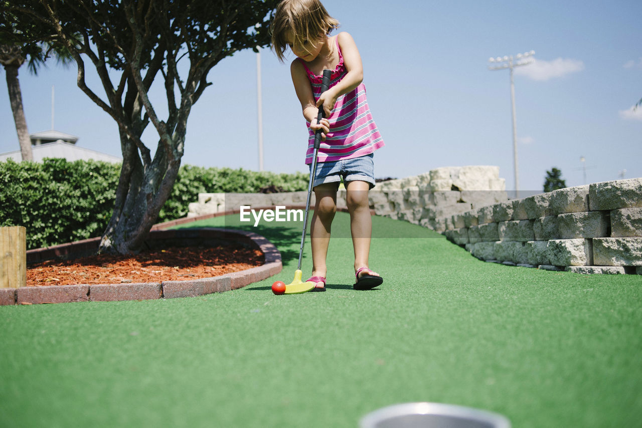 Girl playing miniature golf during sunny day