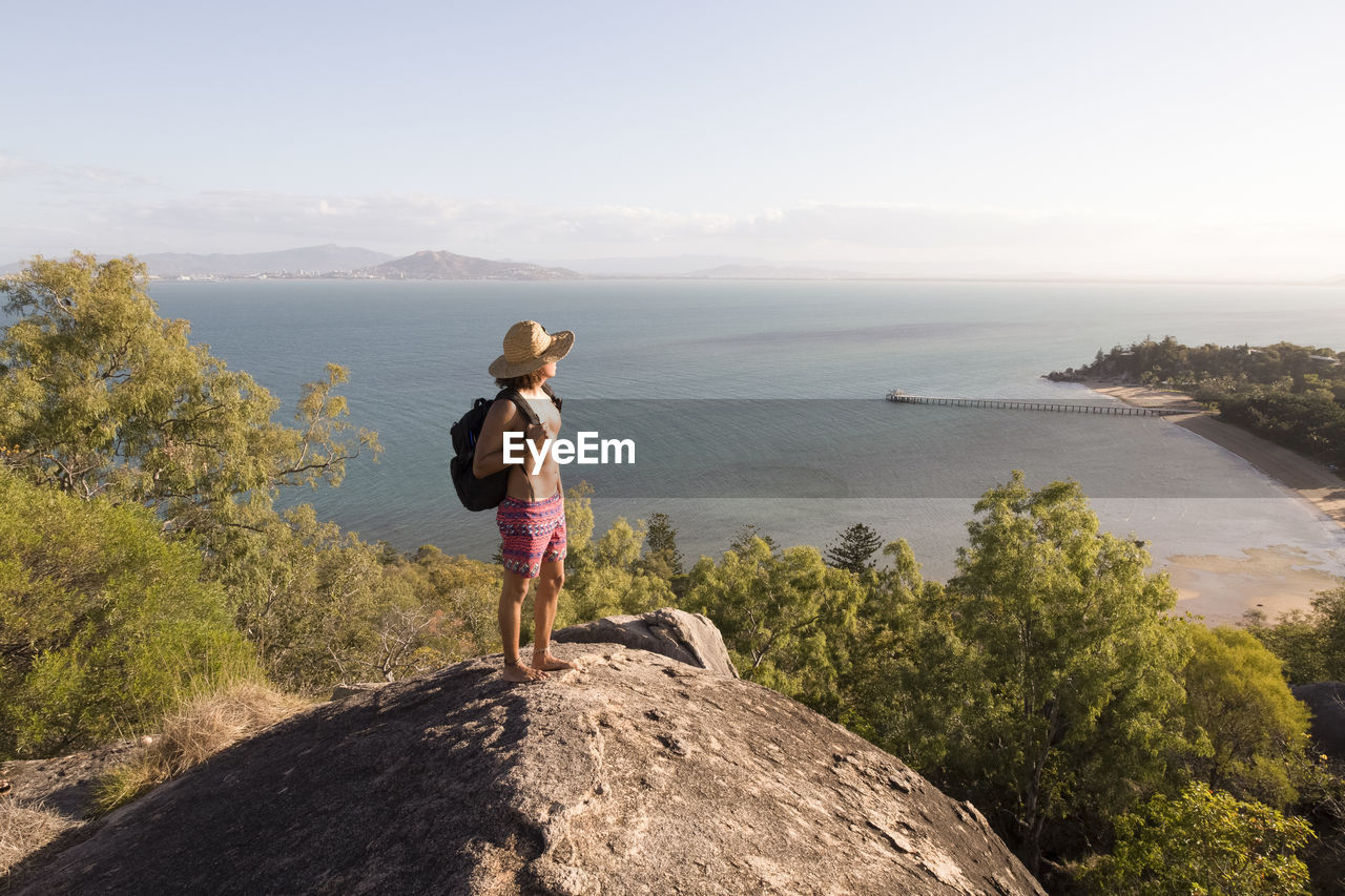 Backpacker with hat and swimsuit, on top of rocky hill during sunset