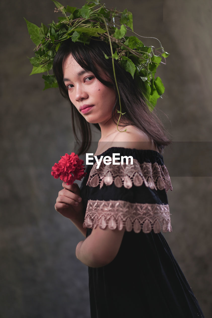 PORTRAIT OF BEAUTIFUL YOUNG WOMAN STANDING BY ROSE