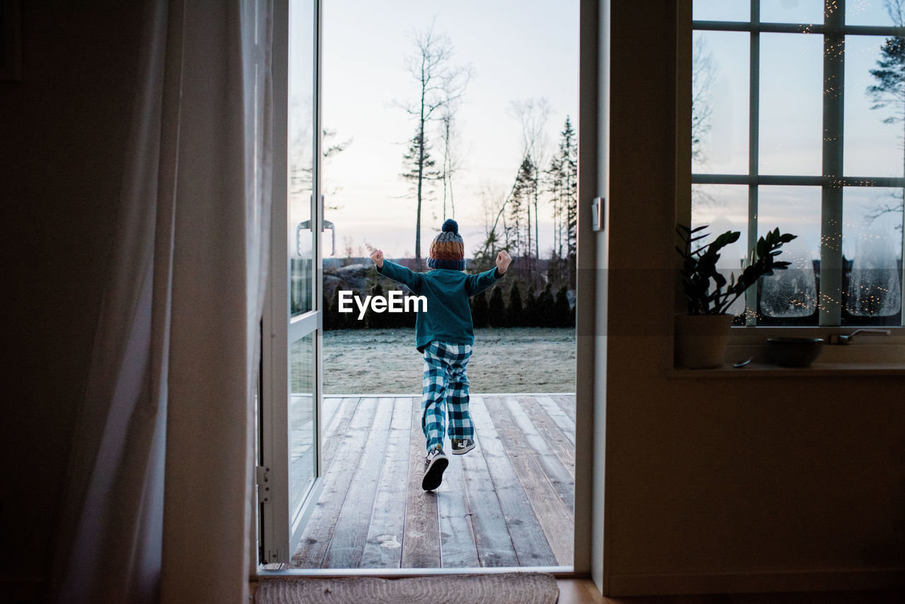 Young boy running out the backdoor to play outside in winter