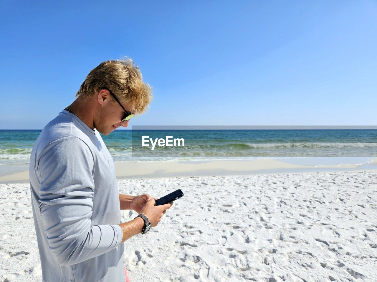 Cute millennial dude texting on beach in summertime.