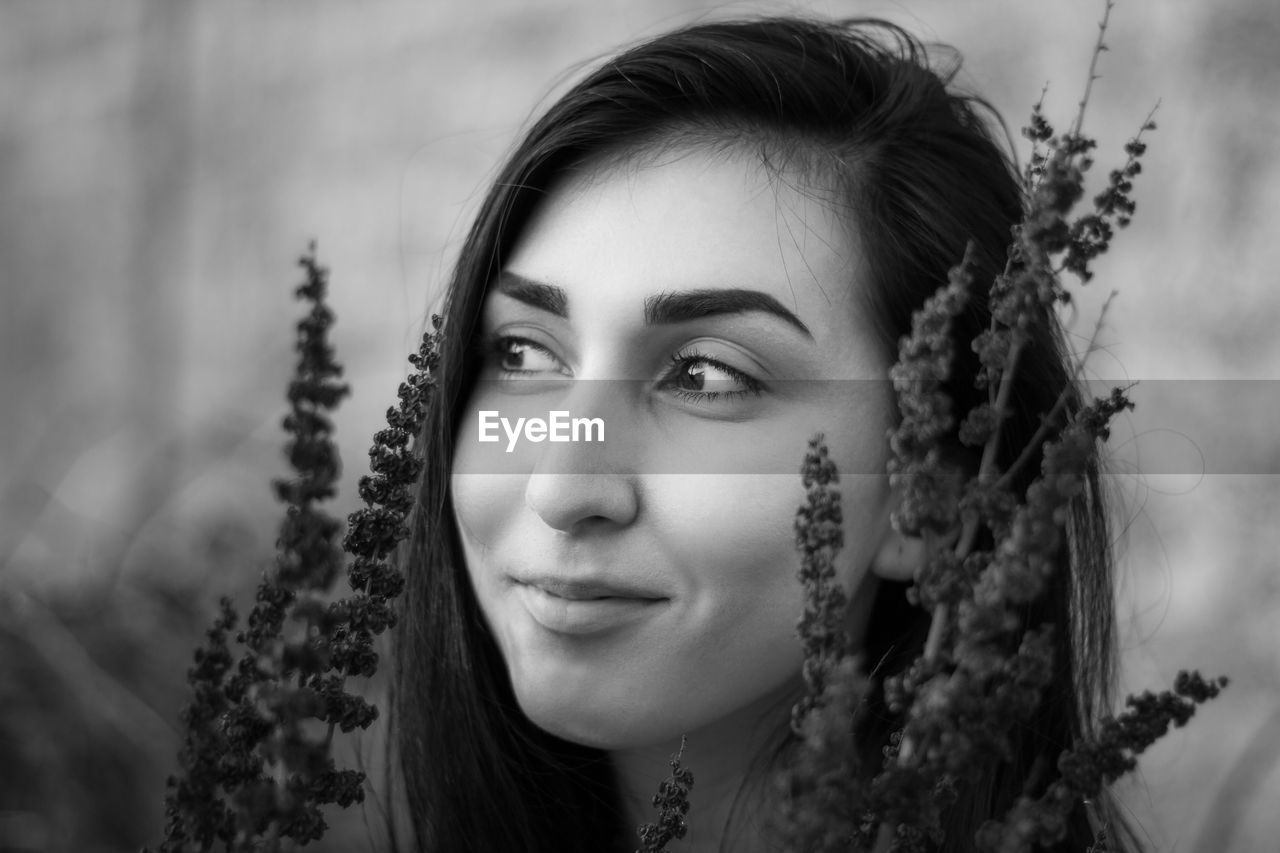 Close-up of smiling young woman looking away by plants