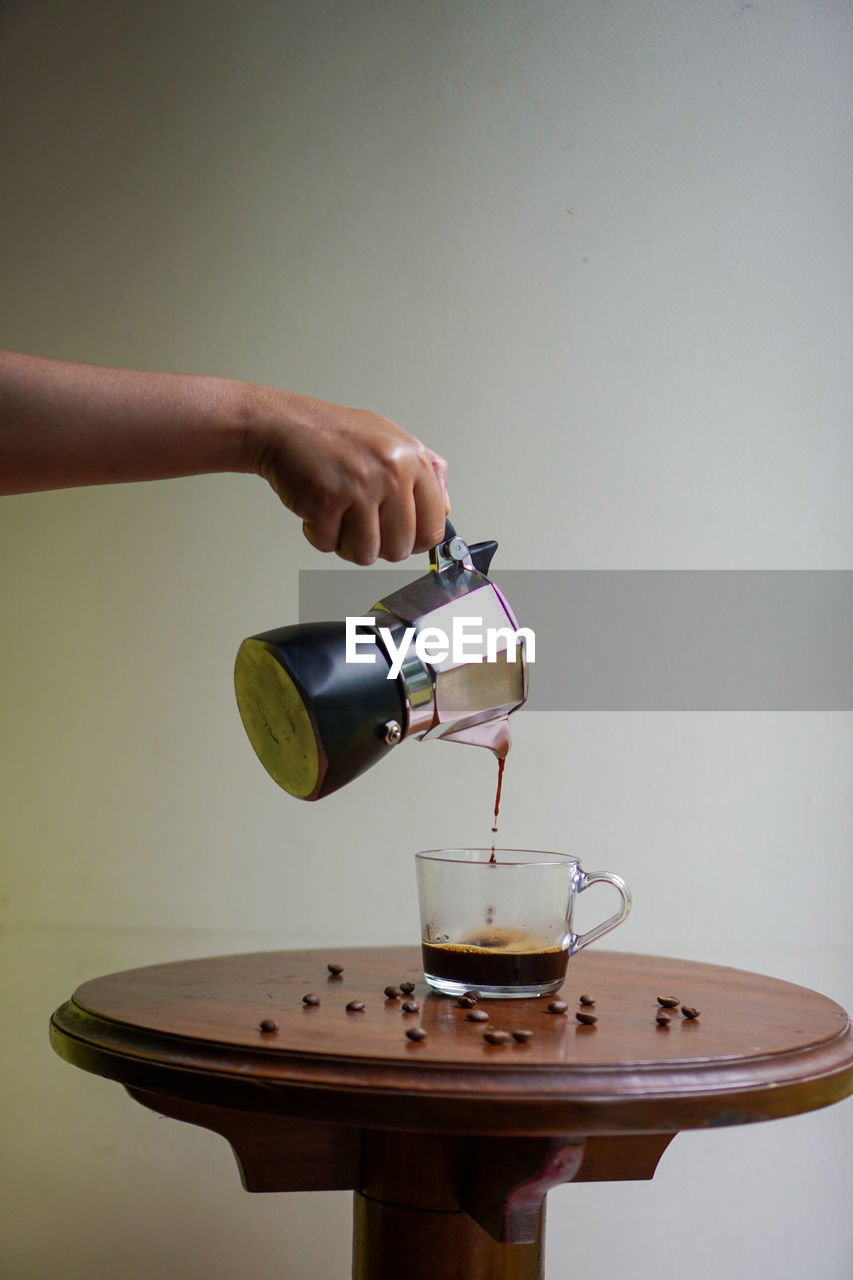 Midsection of person pouring coffee in cup with mokapot