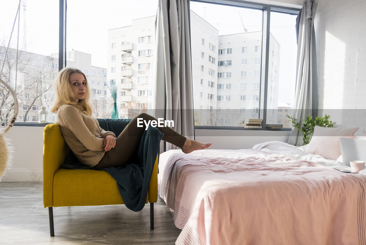 Portrait of woman relaxing on armchair in bedroom at home