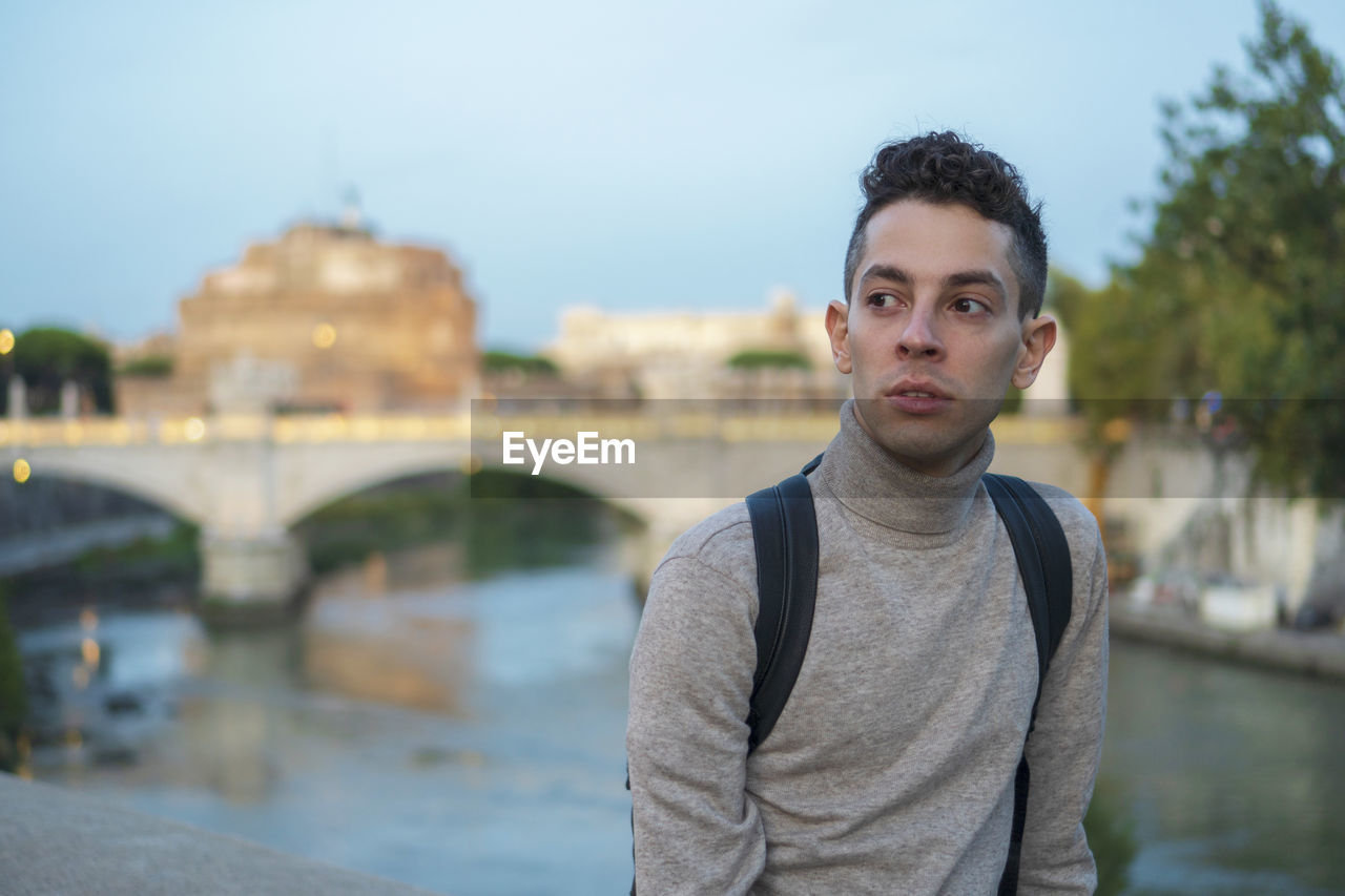 Thoughtful young man standing against bridge over river