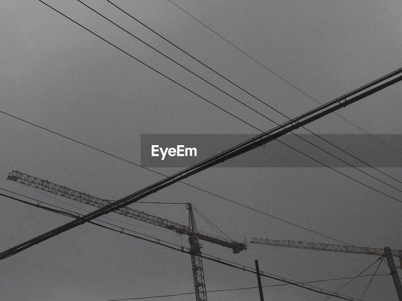 Low angle view of cables by cranes against cloudy sky