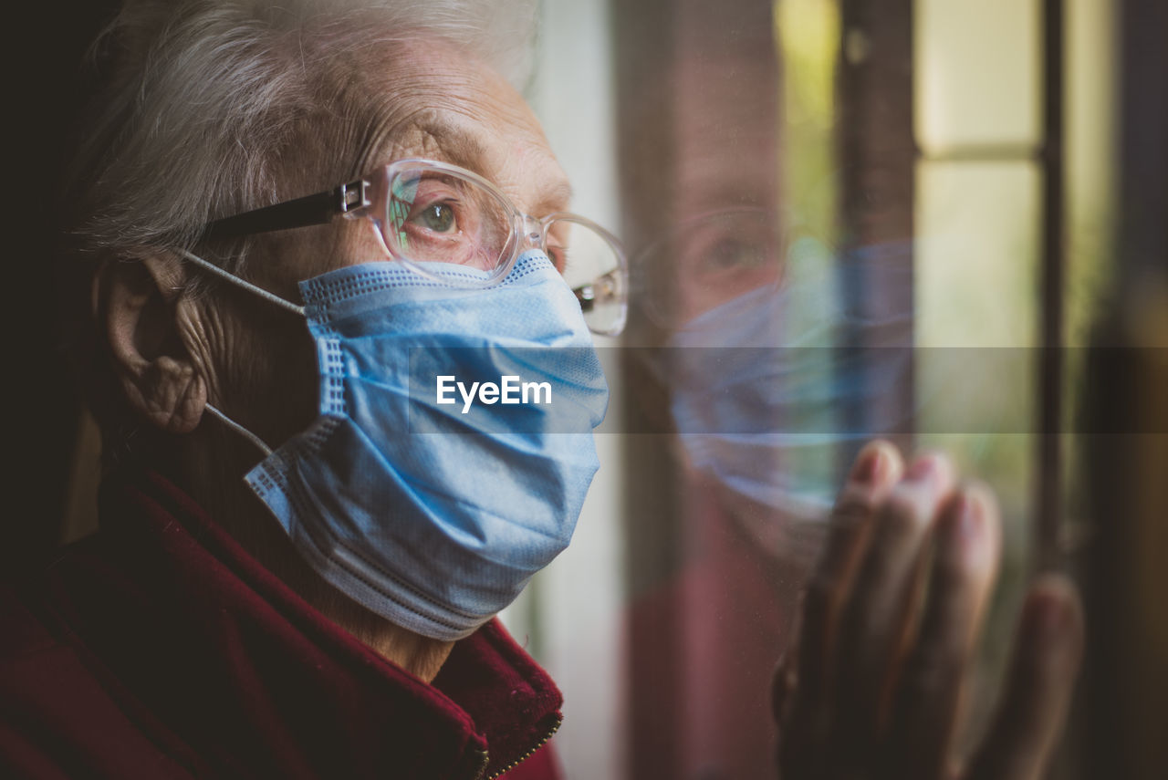 Close-up of senior woman wearing mask with reflection on window