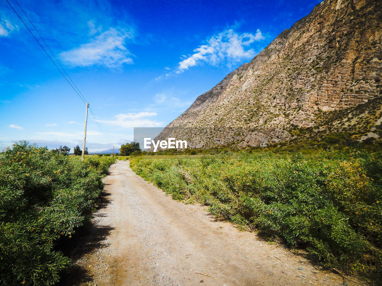 Road passing through field against cloudy sky