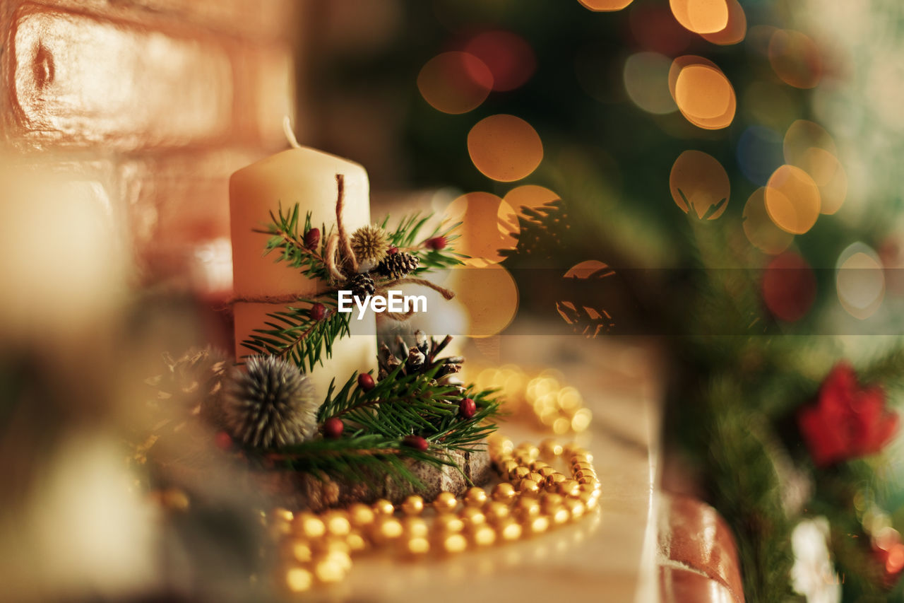 A candle in a christmas candlestick stands on a shelf or fireplace, close-up.