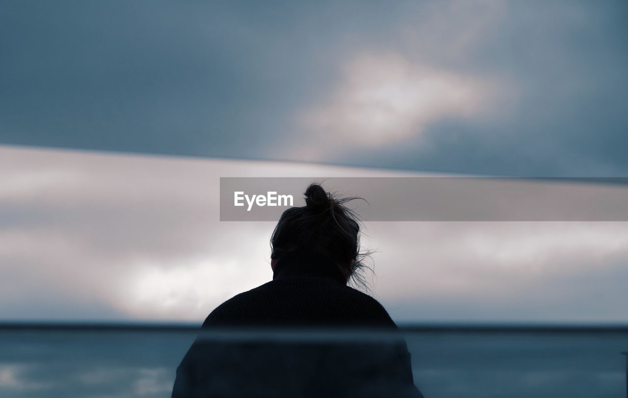 REAR VIEW OF WOMAN LOOKING AT SEA AGAINST SUNSET SKY