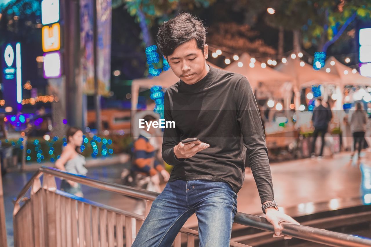 Young man using phone while sitting on railing by staircase 