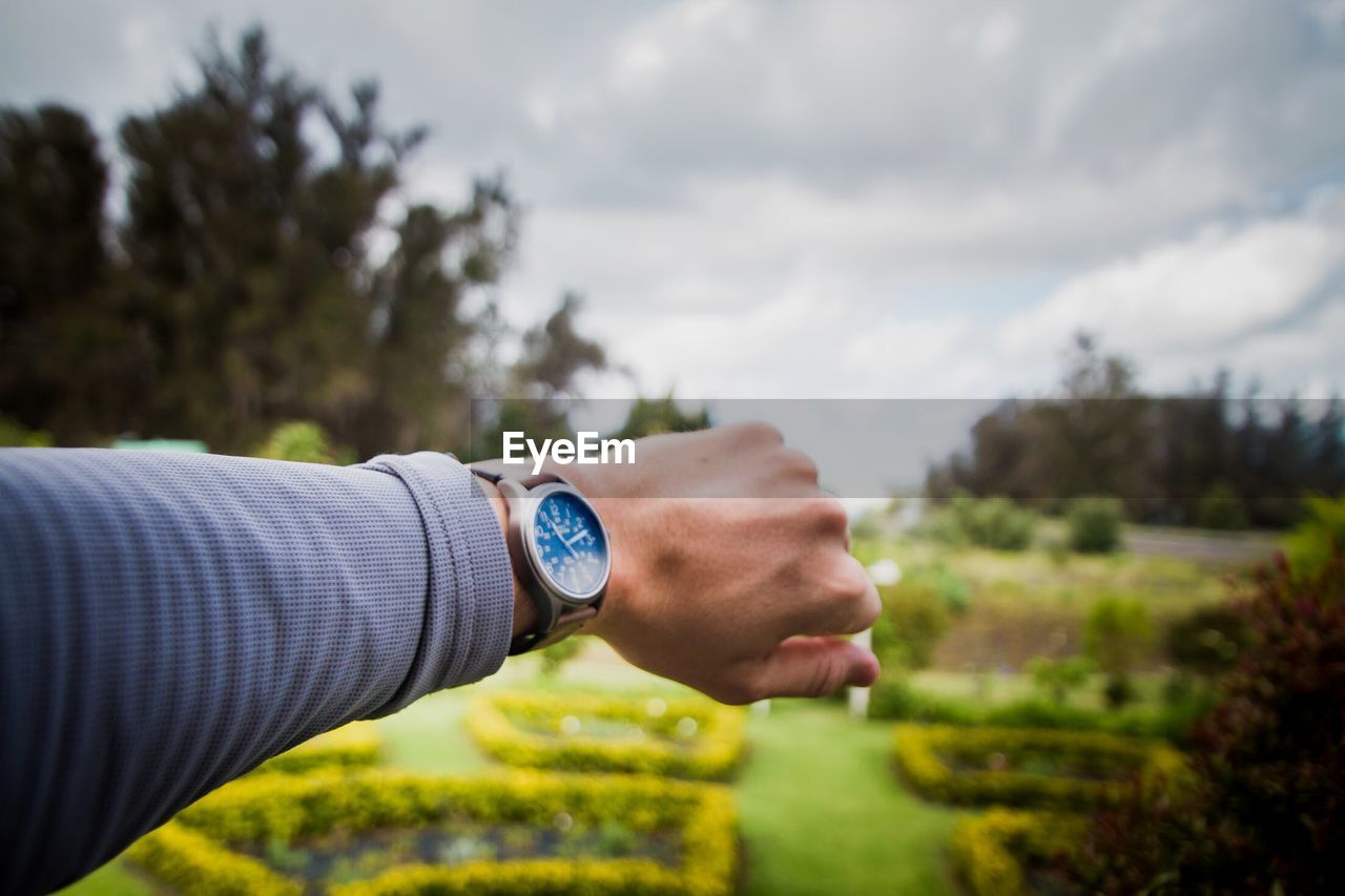 Cropped hand of woman wearing wristwatch against sky