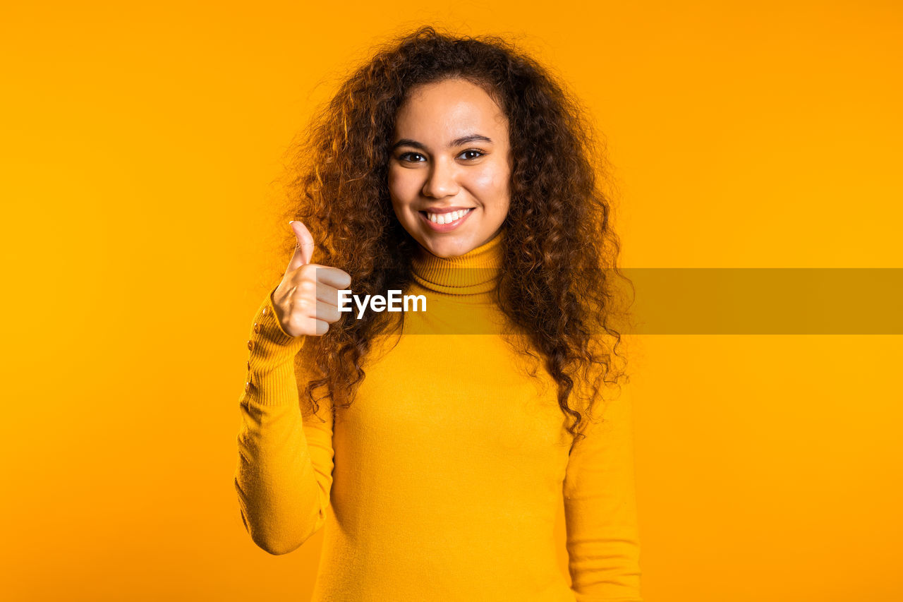 PORTRAIT OF A SMILING YOUNG WOMAN OVER YELLOW BACKGROUND