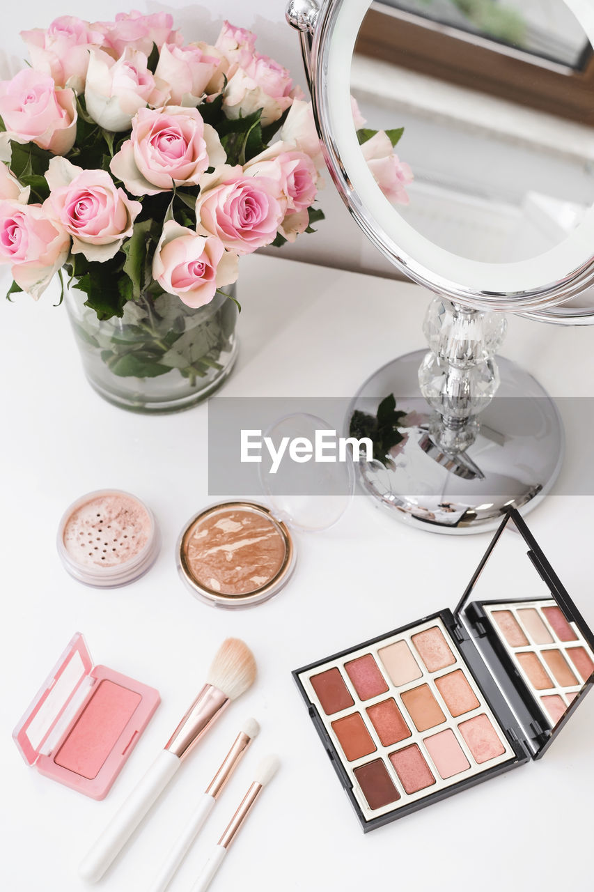 Cosmetics for make-up, round mirror and roses flowers on table. decorative cosmetics, brushes, eyes