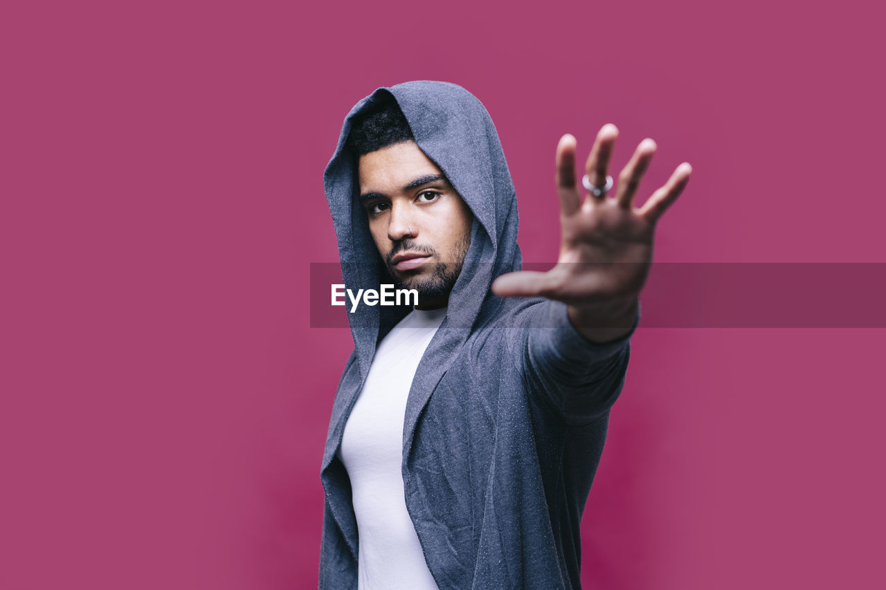 Man in jacket showing stop sign against pink background