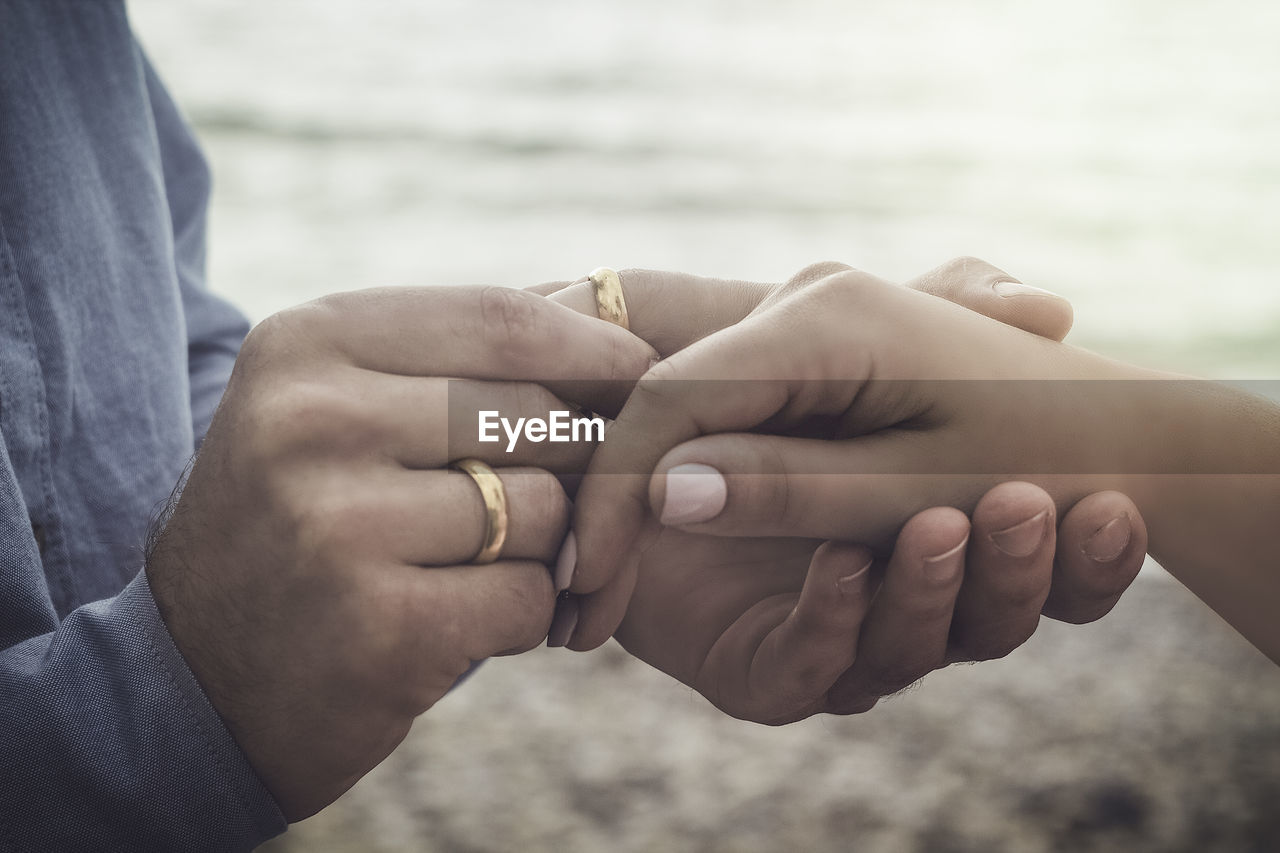 Midsection of man putting engagement ring on woman finger at beach