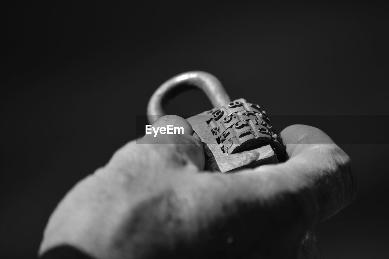Close-up of hand holding padlock with numbers against black background