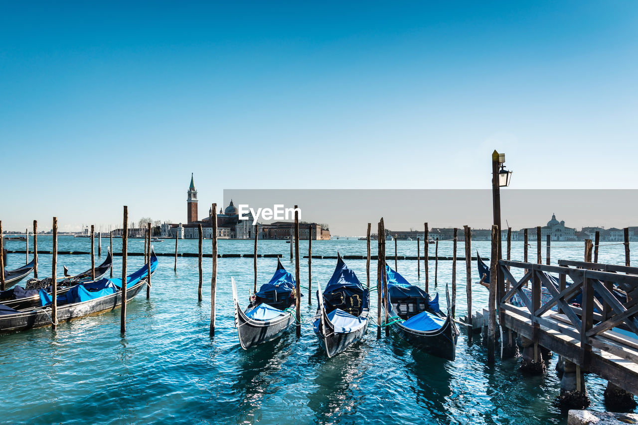 High angle view of gondolas moored in canal against clear blue sky