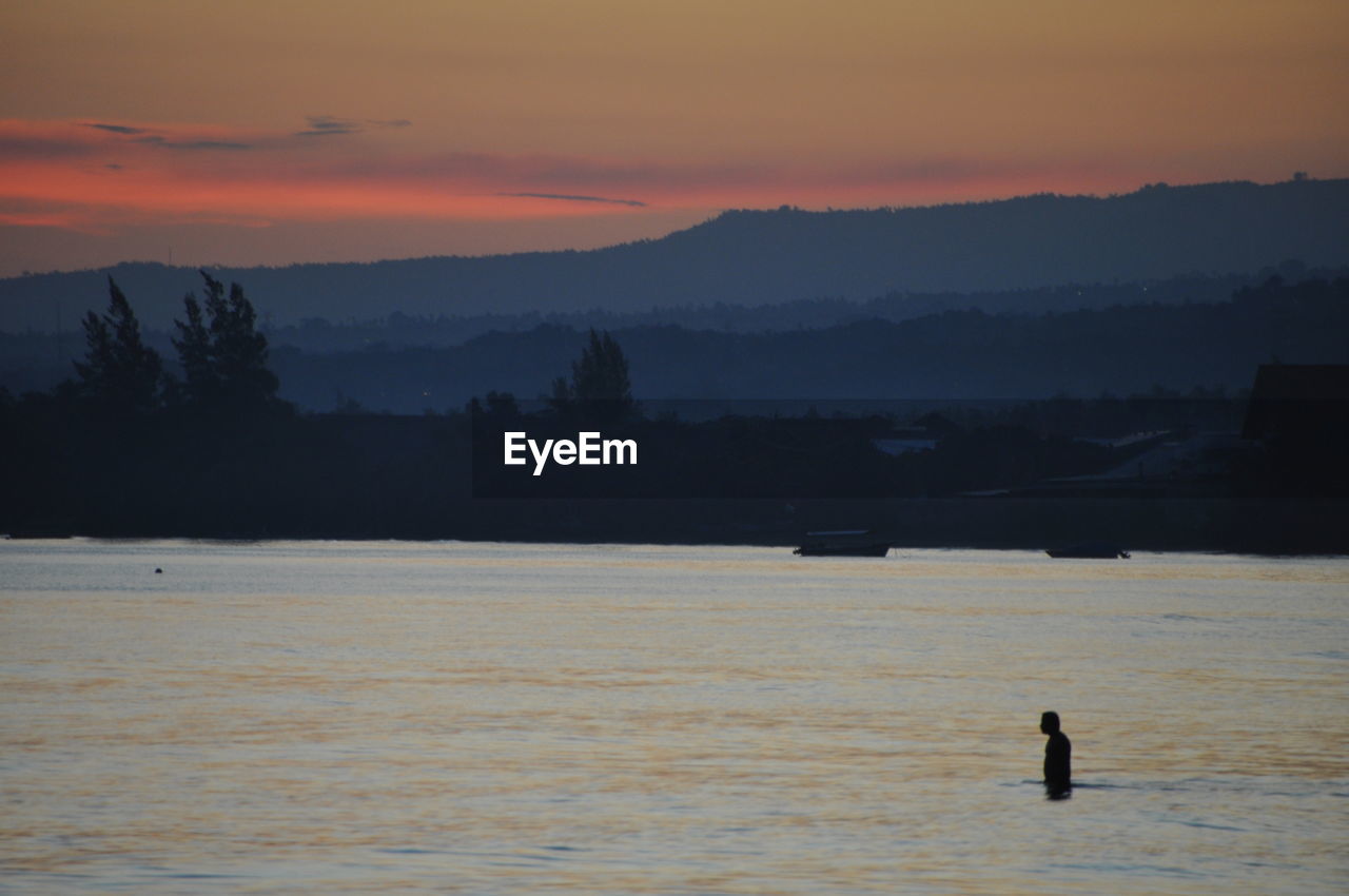 Silhouette man in sea against sky during sunset