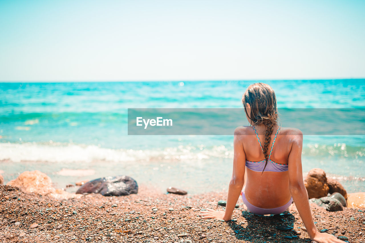 REAR VIEW OF WOMAN LOOKING AT SEA SHORE