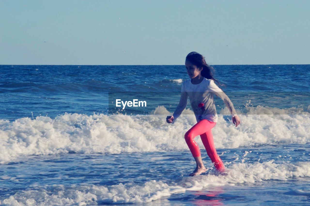 Girl walking on shore at beach against sky