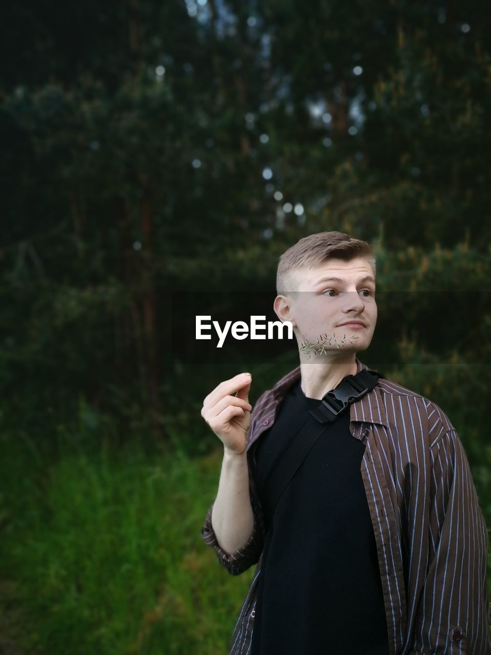 PORTRAIT OF YOUNG MAN LOOKING AWAY AGAINST TREES