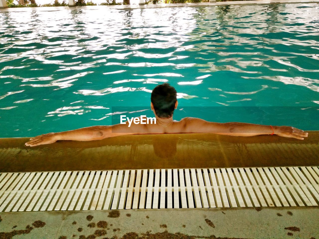 Rear view of shirtless man with arms outstretched in pool