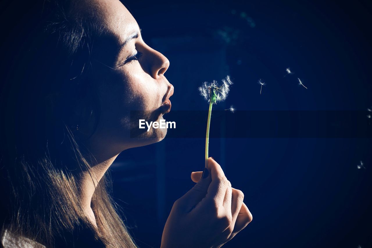 Close-up of woman blowing dandelion during sunset