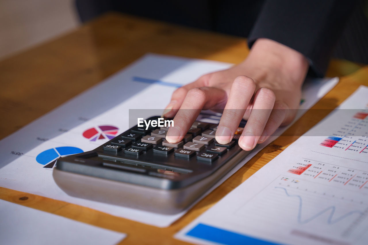 Cropped hand of businesswoman using calculator on desk