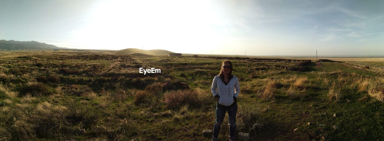 Portrait of mid adult woman standing on grassy field against sky