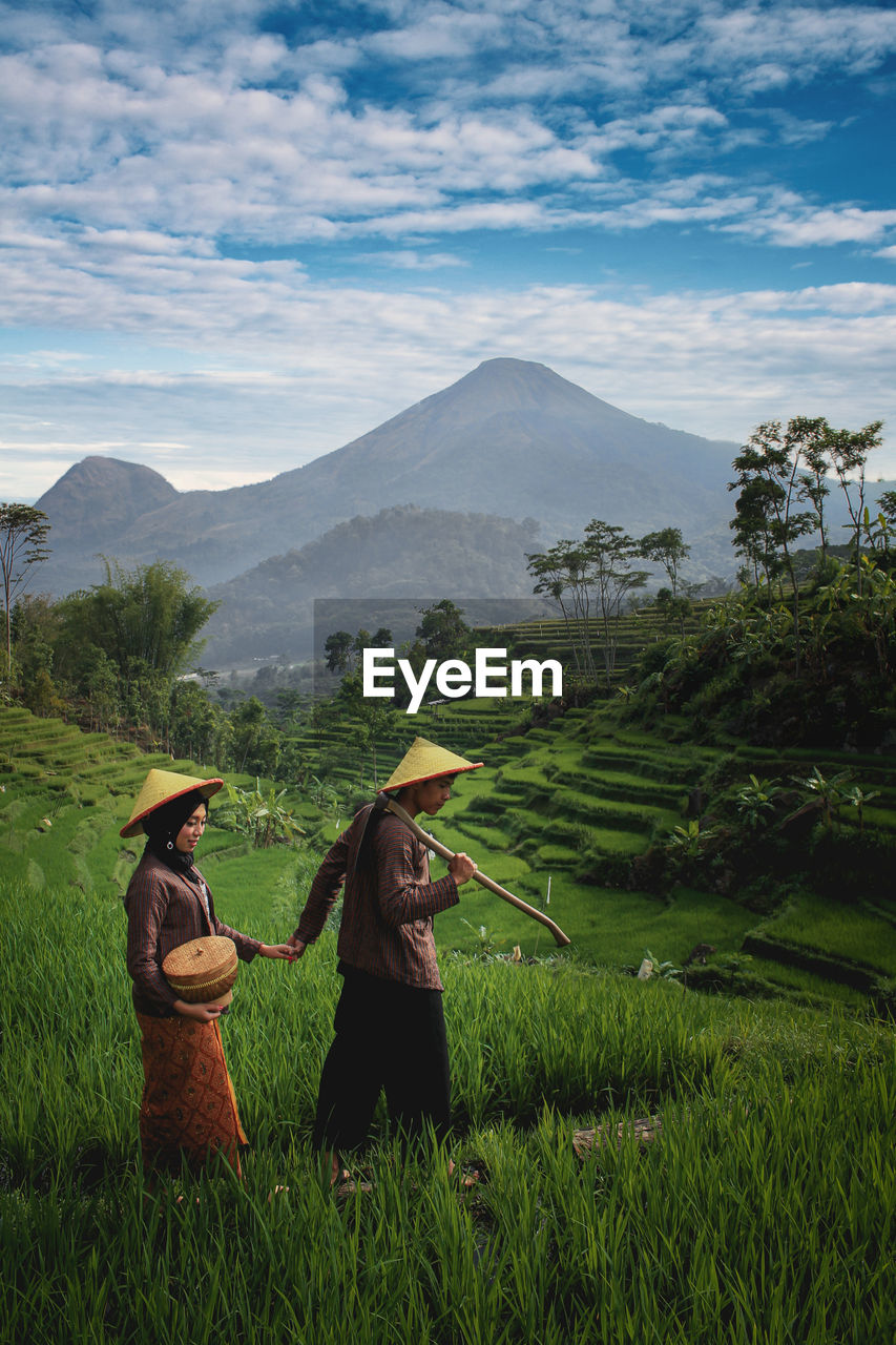 Couple holding hands while walking amidst plants on mountain